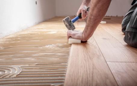 A worker laying wood flooring, ensuring the edges adhere together.