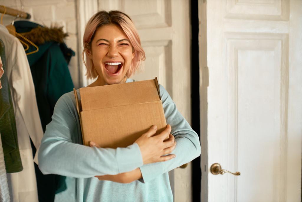 Indoor image of happy young woman holding cardboard box delivered to her apartment.